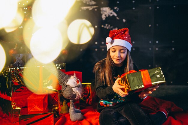 Petite fille assise près d&#39;un arbre de Noël et déballage des cadeaux