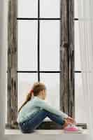 Photo gratuite petite fille assise sur un rebord de fenêtre