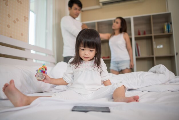 Petite fille assise avec ses parents sur le lit, sérieuse