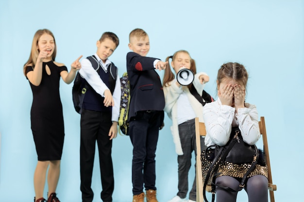 Photo gratuite petite fille assise seule sur une chaise et souffrant d'un acte d'intimidation pendant que les enfants se moquent