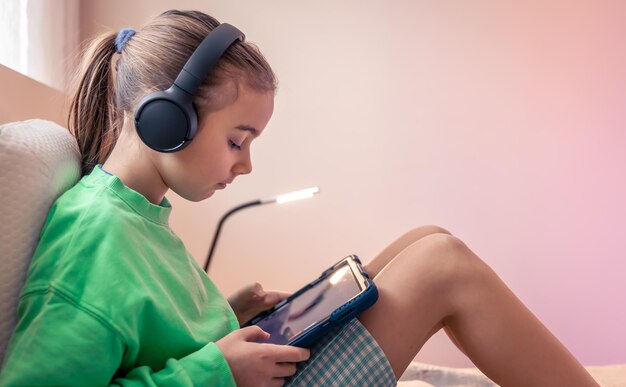 Petite fille au casque avec une tablette dans sa chambre