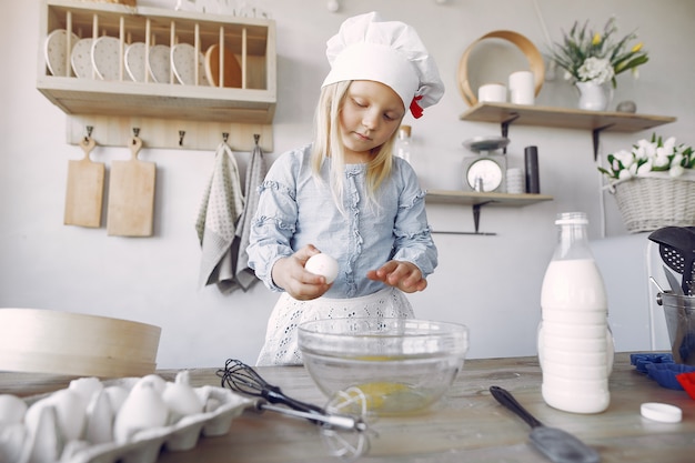 Petite fille au chapeau blanc de shef cuire la pâte pour les biscuits