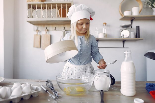 Petite fille au chapeau blanc de shef cuire la pâte pour les biscuits