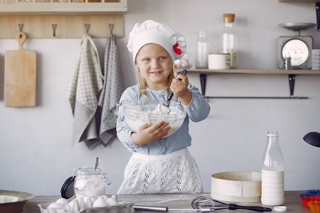 Petite fille au chapeau blanc de shef cuire la pâte pour les biscuits