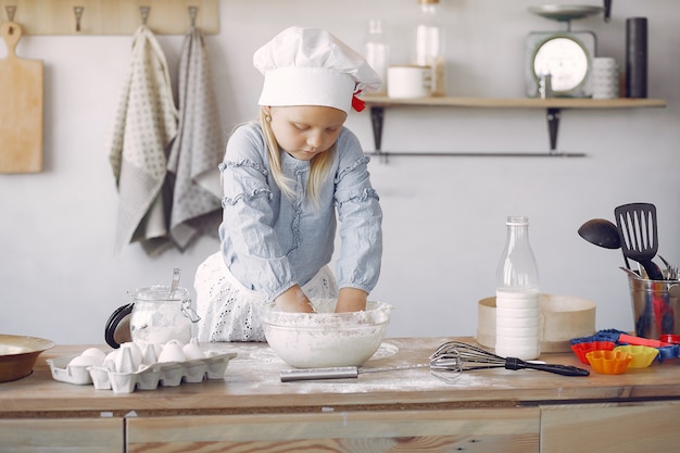 Petite fille au chapeau blanc de shef cuire la pâte pour les biscuits