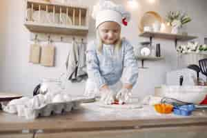 Photo gratuite petite fille au chapeau blanc de shef cuire la pâte pour les biscuits