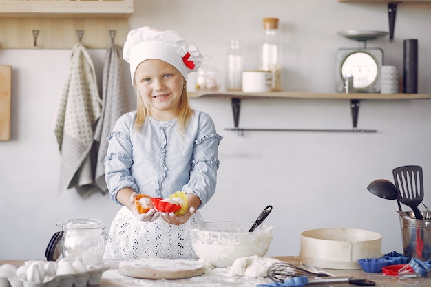 Petite fille au chapeau blanc de shef cuire la pâte pour les biscuits