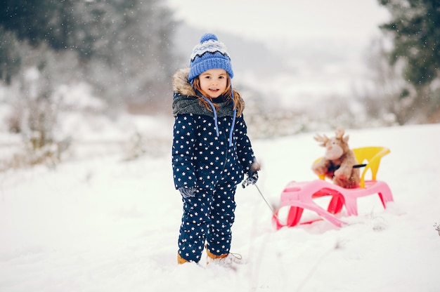 Petite fille au chapeau bleu jouant dans une forêt d'hiver