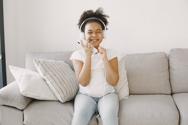 Photo gratuite petite fille aux cheveux bouclés. l'enfant sèche la musique dans les écouteurs. amusez-vous à la maison.