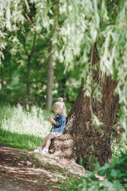 Petite fille blonde assise sur un arbre de manger une crème glacée