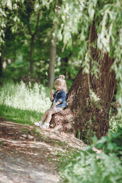 Petite fille blonde assise sur un arbre de manger une crème glacée