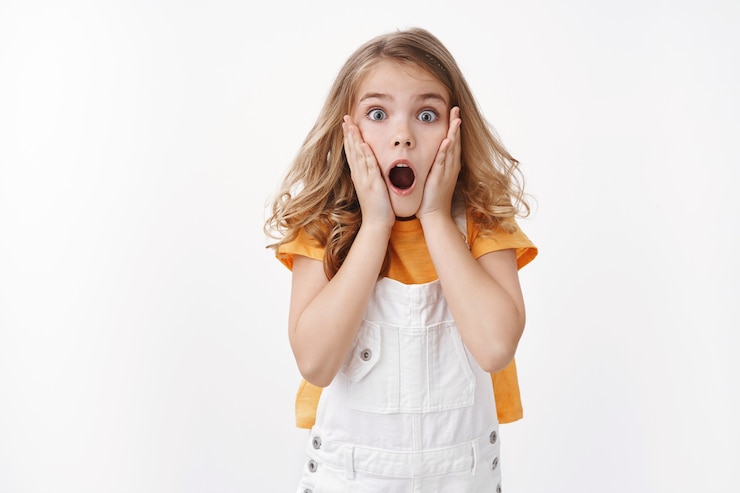 Photo gratuit petite fille blonde caucasienne effrayée et choquée haletant, saisir le visage émerveillé, regarder la caméra étonnée, laisser tomber la mâchoire sans voix observer l'événement secoué, réagir dans une embuscade, effrayée voir l'araignée, mur blanc