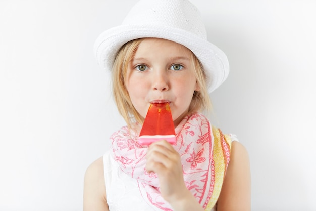 Petite fille blonde portant un chapeau blanc et manger de la crème glacée