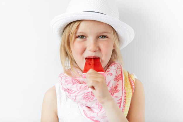 Petite fille blonde portant un chapeau blanc et manger de la crème glacée