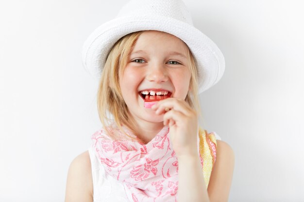 Petite fille blonde portant un chapeau blanc et manger de la crème glacée