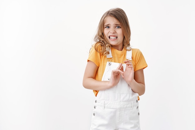 Une petite fille blonde réticente et effrayée aux yeux bleus exprime le dégoût et l'aversion, grince des dents à cause d'une odeur affreuse, lève les mains pour bloquer le refus, rejette une chose dégoûtante, reste debout en grimaçant sur le mur blanc