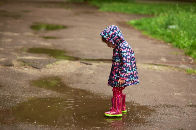 Petite fille en bottes en caoutchouc s&#39;amuse à marcher dans les piscines après la pluie