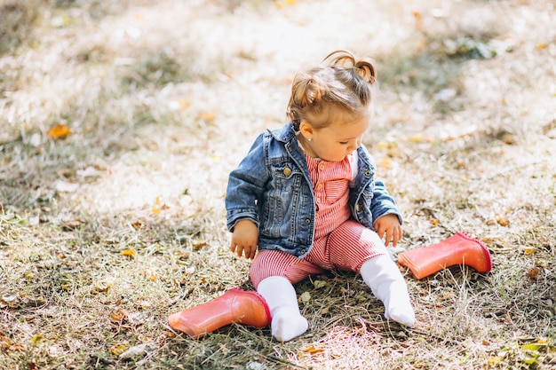 Petite fille avec des bottes de pluie assis dans un parc