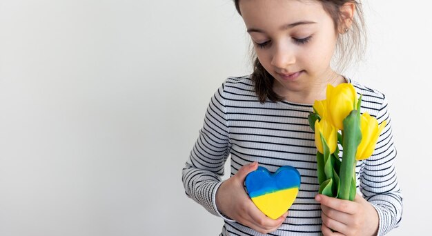 Petite fille avec un bouquet de tulipes et un coeur avec le drapeau de l'ukraine