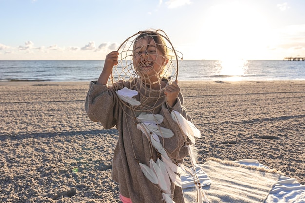 Photo gratuite petite fille avec un capteur de rêves au bord de la mer au coucher du soleil