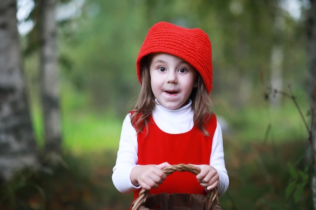 Une petite fille avec un chapeau rouge et des robes marche dans le parc. cosplay pour le héros de conte de fées 