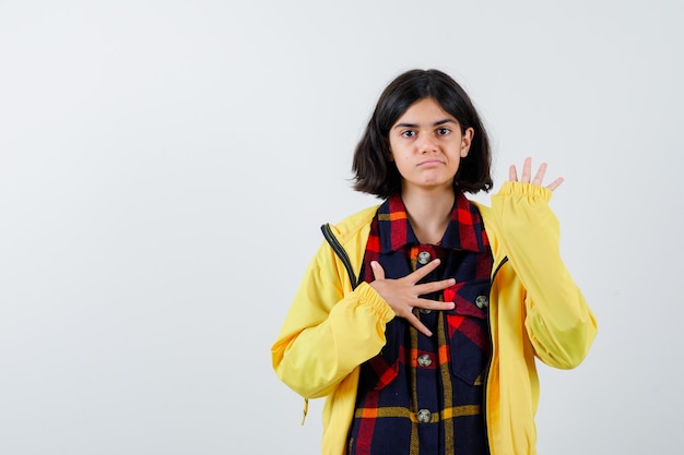 Petite fille en chemise à carreaux, veste montrant la paume et à la confiance