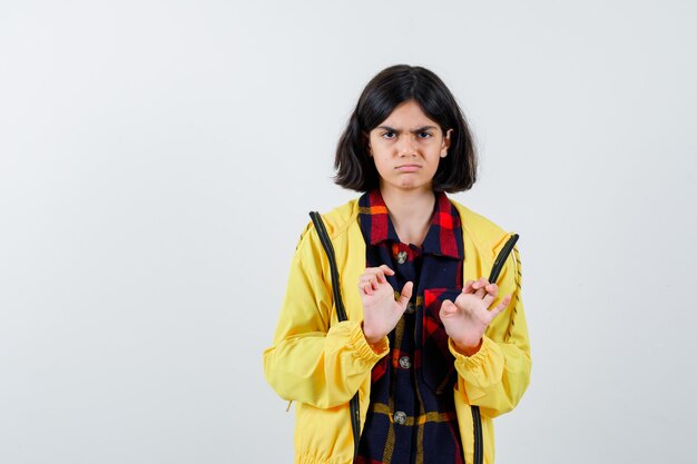 Petite fille en chemise à carreaux, veste montrant les paumes en geste de reddition et à désespérément