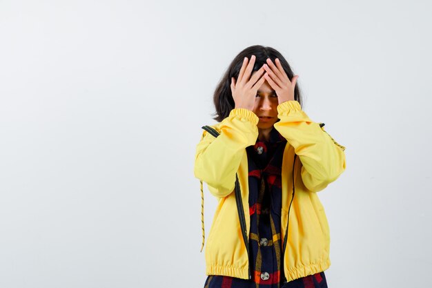 Petite fille en chemise à carreaux, veste tenant les mains sur le front et à la recherche d'oubli