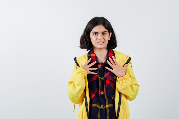 Petite fille en chemise à carreaux, veste tenant les mains sur la poitrine et à la jolie