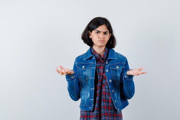 Petite fille en chemise, veste montrant un geste impuissant et l'air sombre, vue de face.