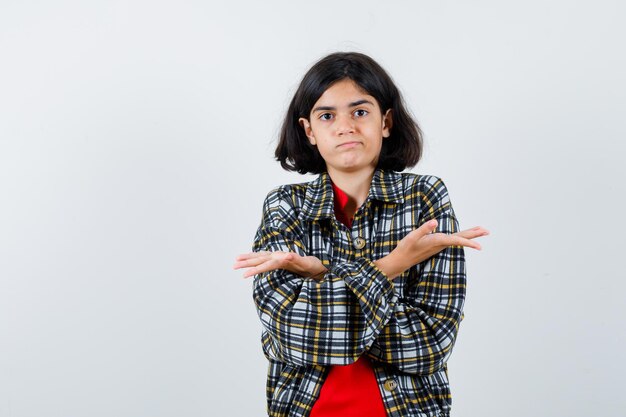 Petite fille en chemise, veste montrant un geste impuissant avec les mains croisées et l'air confus, vue de face.