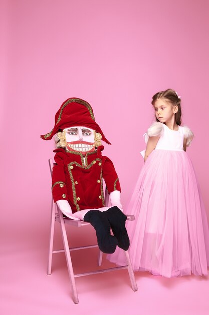 Une petite fille comme ballerine de beauté à longue robe rose avec casse-noisette au studio rose
