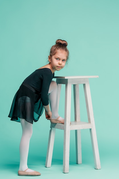 La Petite Fille Comme Danseuse Balerina Près De Chaise Sur Studio Bleu