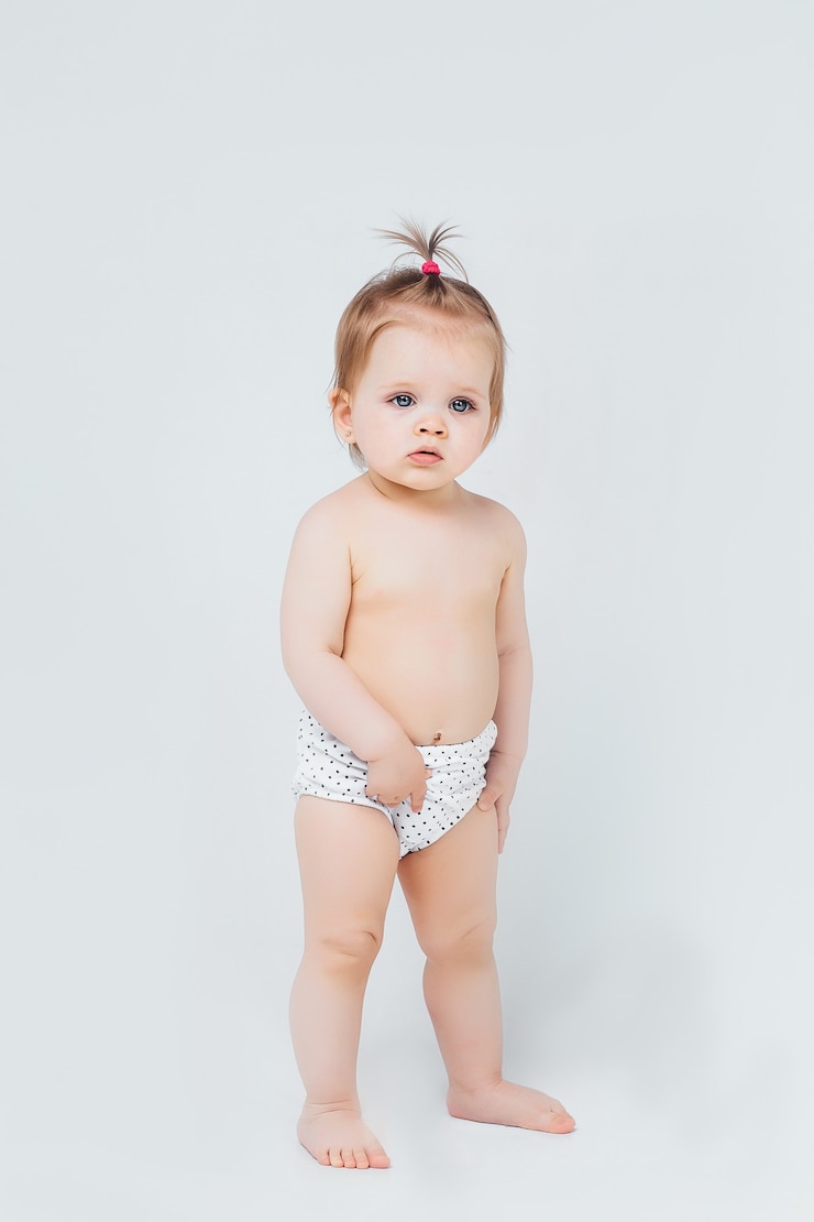 Photo gratuit une petite fille en couche est assise heureuse et sourit sur un mur blanc.