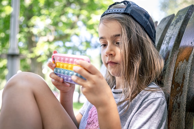 Petite fille dans une casquette avec un smartphone dans un étui dans le style des jouets anti stress pop it.