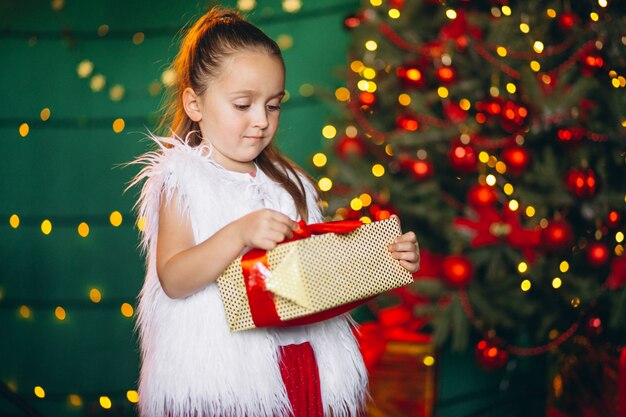 Petite fille déballage cadeau par arbre de Noël