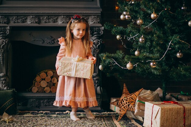 Petite fille déballant les cadeaux de Noël par sapin de Noël