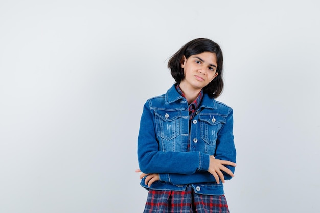 Petite fille debout avec les bras croisés en chemise, veste et l'air confiant, vue de face.