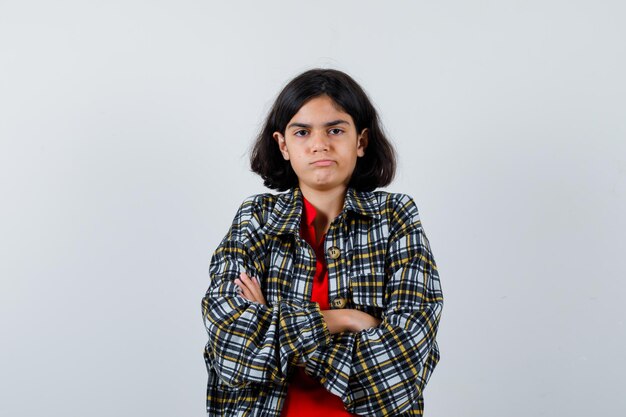 Petite fille debout avec les bras croisés en chemise, veste et l'air offensé. vue de face.