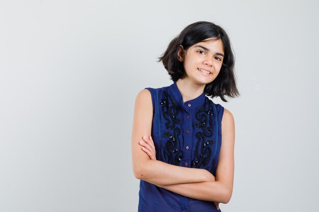 Petite fille debout avec les bras croisés en chemisier bleu et à la joyeuse.