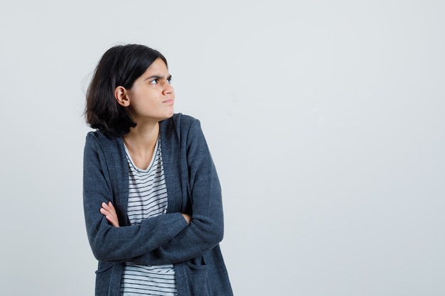 Petite fille debout avec les bras croisés en t-shirt, veste et à la perplexe