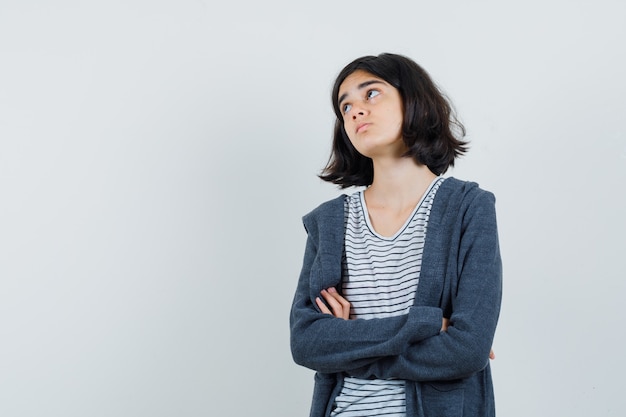 Petite fille debout avec les bras croisés en t-shirt, veste et à la recherche attentionnée.