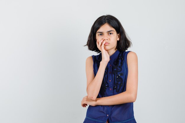 Petite fille debout dans la pensée pose en chemisier bleu et à la colère