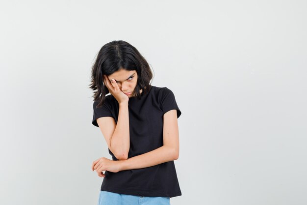 Petite fille debout dans la pensée pose en t-shirt noir, short et à la vue offensée, de face.