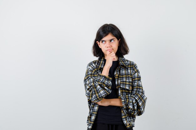 Petite fille debout en pensant pose en t-shirt, veste et regardant pensive, vue de face.