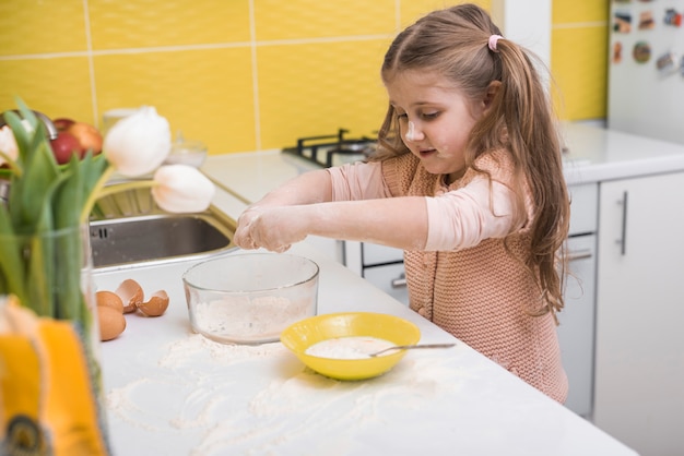 Petite fille debout à la table avec un bol de farine