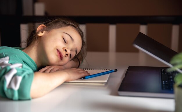 Petite fille dort devant un ordinateur portable sur la table