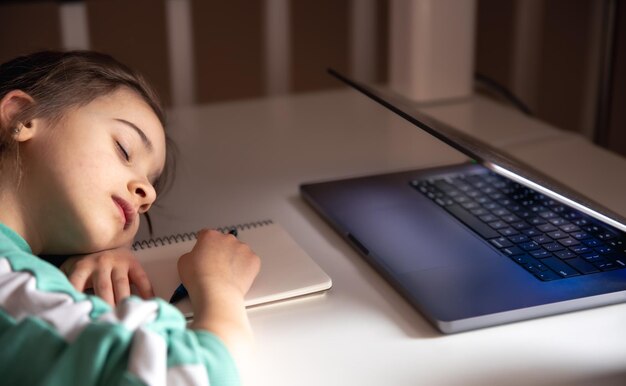 Petite fille dort devant un ordinateur portable sur la table