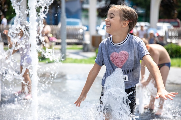 Petite fille drôle dans une fontaine, parmi les éclaboussures d'eau par une chaude journée d'été.