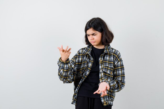 La petite fille écarte les paumes dans un geste désemparé en t-shirt, veste et à l'air hésitant. vue de face.